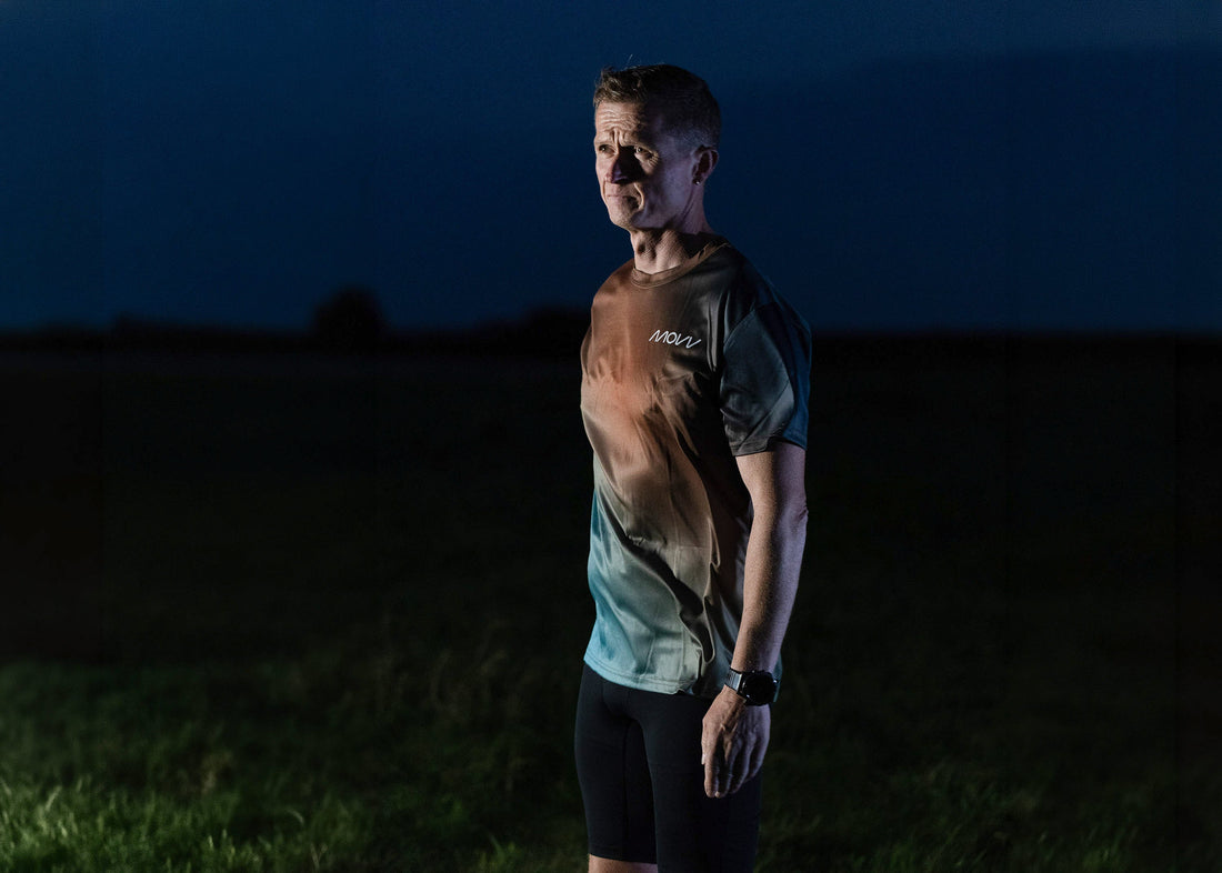 Ultra runner Danni in a MOVV running shirt, standing in a field at dusk under a deep blue sky.