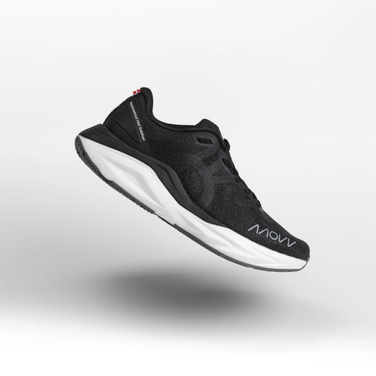 A black athletic running shoe with white midsole photographed against a light gray background. The shoe features a dark mesh upper material, black laces, and MOVV branding visible on the side.