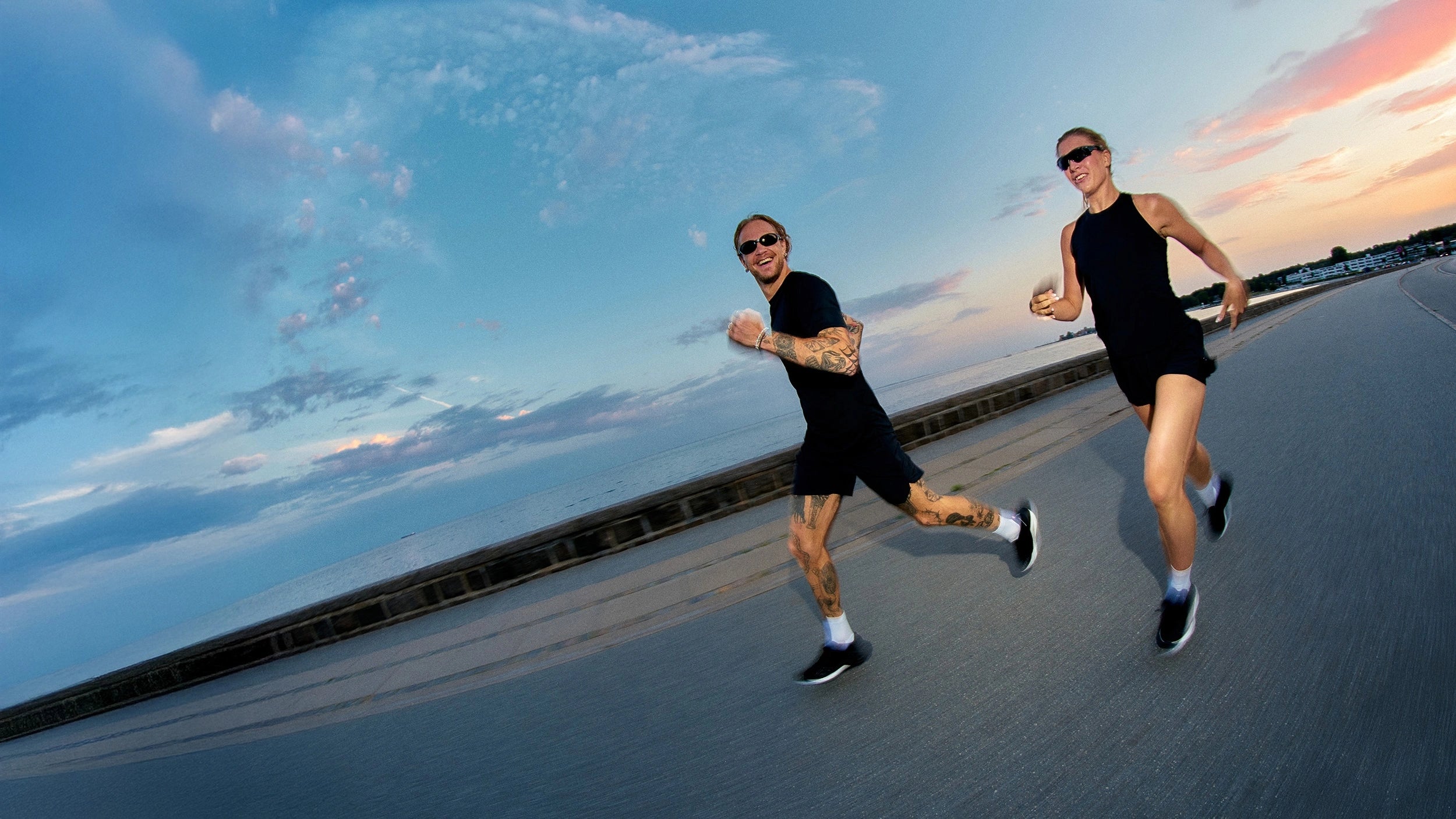 Man and woman running by the ocean at sunset in black athletic wear and MOVV Solara running shoes. 